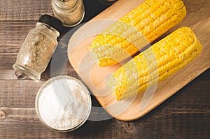 Corn. Appetizing boiled corn with salt and seasonings on a wooden table. Top view