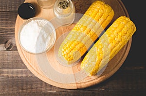 Corn. Appetizing boiled corn with salt and seasonings on a wooden table. Top view