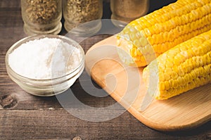 Corn. Appetizing boiled corn with salt and seasonings on a wooden table. Top view