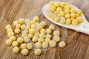 Corn balls in white spoon, scattered corn balls on wooden table