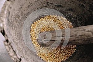 Corn being grinded with mortar and pestle made of wood to produce flour.