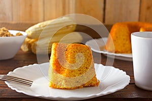 Corn cake sliced on white plate on rustic wooden table. Typical Brazilian food. Front view