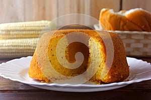 Corn cake sliced on white plate on rustic wooden table. Typical Brazilian food. Front view