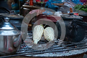 Corn cobs and tea kettles being heated on charcoal grill