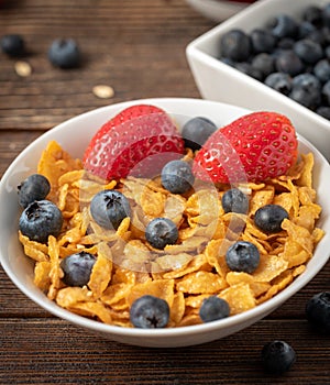 Corn flakes with blueberries and raspberries in white bowl in dark wooden desk