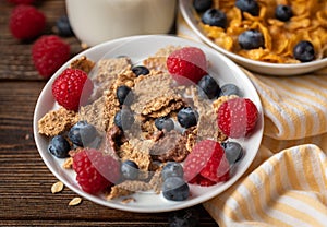 Corn flakes with blueberries and raspberries in white bowl in dark wooden desk