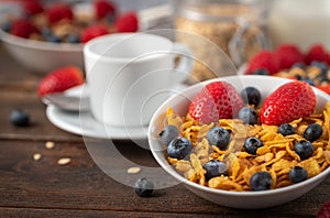 Corn flakes with blueberries and raspberries in white bowl in dark wooden desk