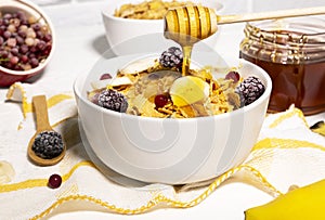 Corn Flakes Bowl with Honey, Banana, Berries and Wooden Spoon on white background, Healthy Breakfast, Delicious Food