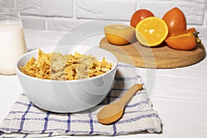 Corn Flakes Bowl with Milk, Persimmon, Orange and Wooden Spoon on white background, Healthy Breakfast