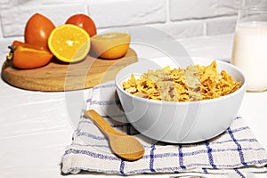 Corn Flakes Bowl with Milk, Persimmon, Orange and Wooden Spoon on white background, Healthy Breakfast