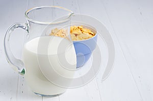 Corn flakes and milk in a glass jug. White wooden table. Copy space