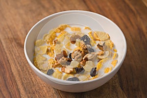 Corn flakes with nuts and fruits in white bowl on wood table