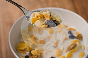 Corn flakes with nuts and fruits in white bowl on wood table