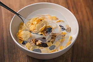 Corn flakes with nuts and fruits in white bowl on wood table