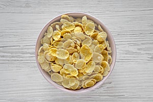 Corn flakes in a pink bowl for breakfast on a white wooden table, top view. Flat lay, overhead, from above. Close-up