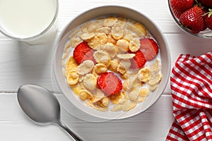 Corn flakes with strawberries in bowl served on wooden table, flat lay