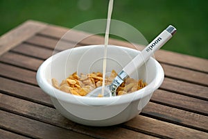 Corn flakes in white bowl spoon inside adding milk