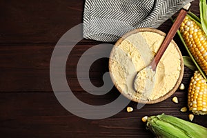 Corn flour in bowl and fresh cobs on wooden table, flat lay. Space for text