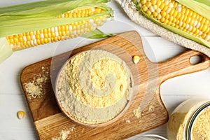 Corn flour in bowl on white wooden table, flat lay