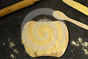 Corn flour on a wooden board, fresh corn on a dark background. The concept of the production of products from corn. Top view