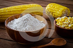 Corn flour in wooden bowl and corn cobs on table