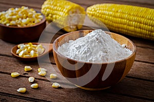 Corn flour in wooden bowl and corn cobs on table