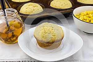 Corn muffin in plate with muffins in pan, syrup and corn in a bo