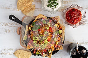 Corn nachos topped with ground beef, melted cheese, vegetables, and guacamole in a cast iron skillet