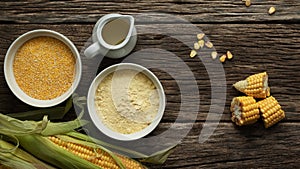 Corn oil, polenta corn grits, corn flour in a porcelain bowl on a wooden table. Ears of corn and slices of corn next to bowls.