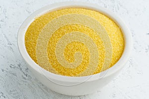 Corn, polenta in white bowl on white background. Dried cereals in cup, vegan food, fodmap diet. Side view, close up