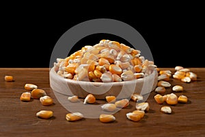 Corn seeds in wooden dish on black background
