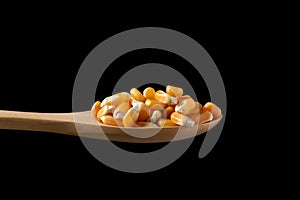 Corn seeds in wooden spoon on black background