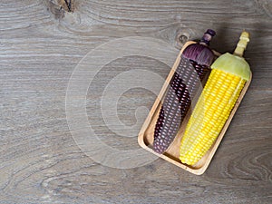 The corn stalks boiled and delicious on the wooden dish and the dish on wooden table. The color of corn is yellow and brown. copy