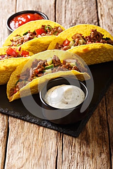 Corn tacos filled with minced beef and vegetables served with sauces close-up. vertical