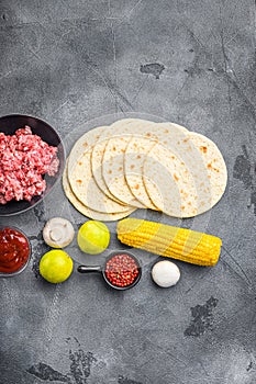 Corn tortilla near raw organic mexican tacos ingredients with  avocado, salsa, chilli and meat. On grey concrete background, top