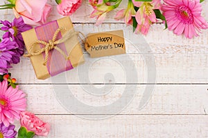Corner border of flowers with Mothers Day gift and tag against white wood