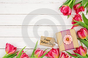 Happy Mothers Day gift and tag with corner border of pink flowers against a white wood background