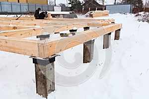 Corner of concrete pile foundation with floor board from square-sawn timber, several carpenters working