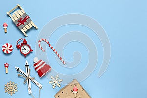 Corner creative Christmas composition. Candy cane, gift in craft paper, sled with deer, hat, alarm clock, ski, clothespins, wooden