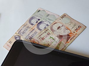 corner of an electronic tablet and uruguayan money on the table