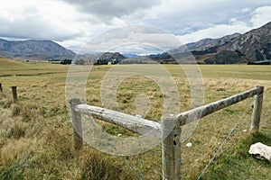 Corner fence strainers and farmland leading to mountains under cloudy sky