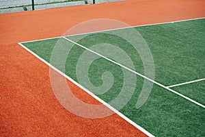 Corner of a green inner tennis court with white markings and brown outer part