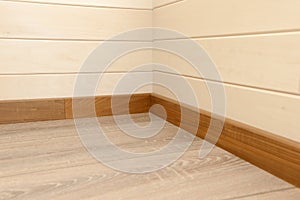 Corner of the house covered with wooden panels, wooden skirting board and wooden floor