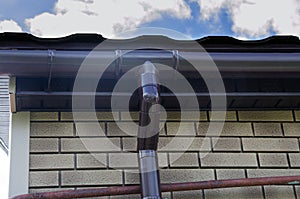 Corner of the house with new gray metal tile roof and rain gutter. Metallic Guttering System, Guttering and Drainage