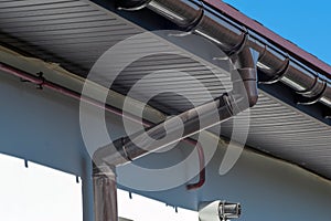 Corner of the house with new gray metal tile roof and rain gutter. Metallic Guttering System, Guttering and Drainage