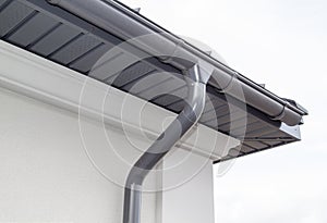 Corner of the house with new gray metal tile roof and rain gutter. Metallic Guttering System, Guttering & Drainage Pipe Exterior photo