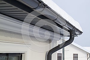 Corner of the house with new gray metal tile roof and rain gutter at winter. Metallic Guttering System, Guttering and Drainage