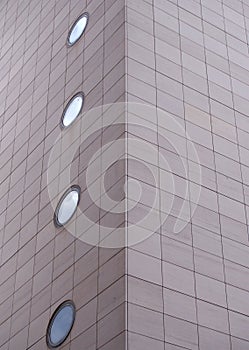 Corner of a large modern commercial building with grey rectangular cladding and round windows