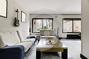 Corner of a living room with a low wooden coffee table with fabric two-seater sofas, twin windows overlooking a terrace
