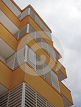 Corner looking upwards view of the corner of a modern apartment building in yellow and white with exterior window blinds against